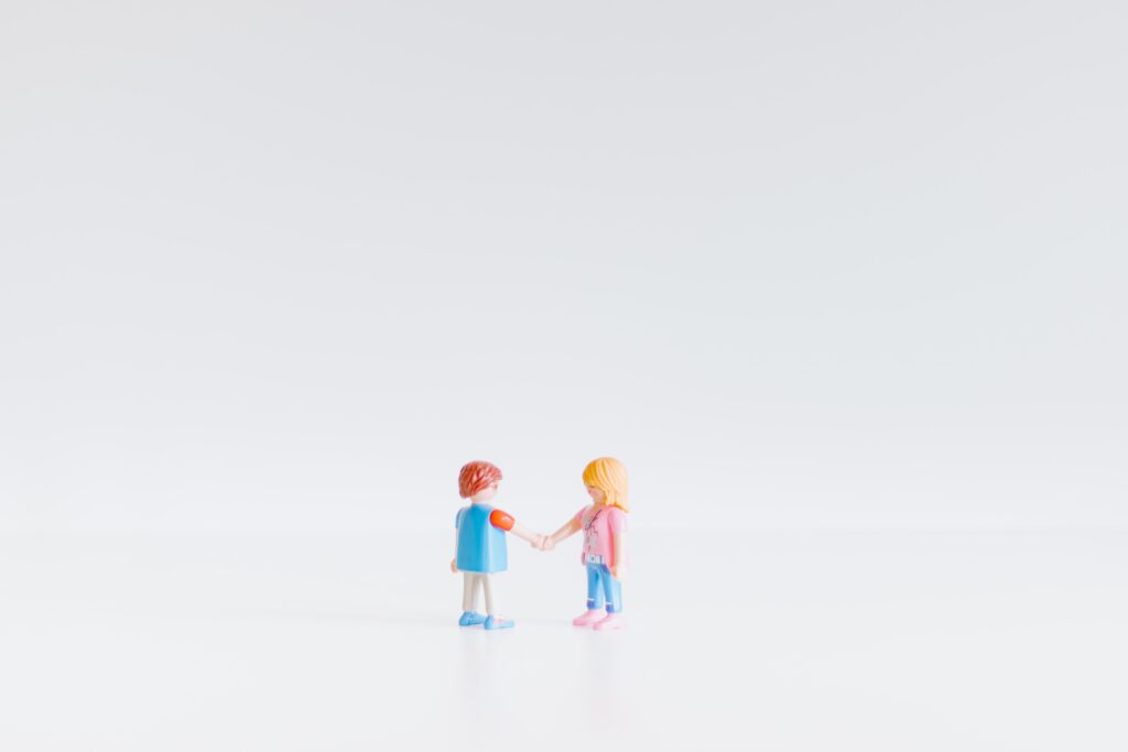 A photo of two tiny play figures shaking hands in agreement. One boy and one girl figure in the center of the image.