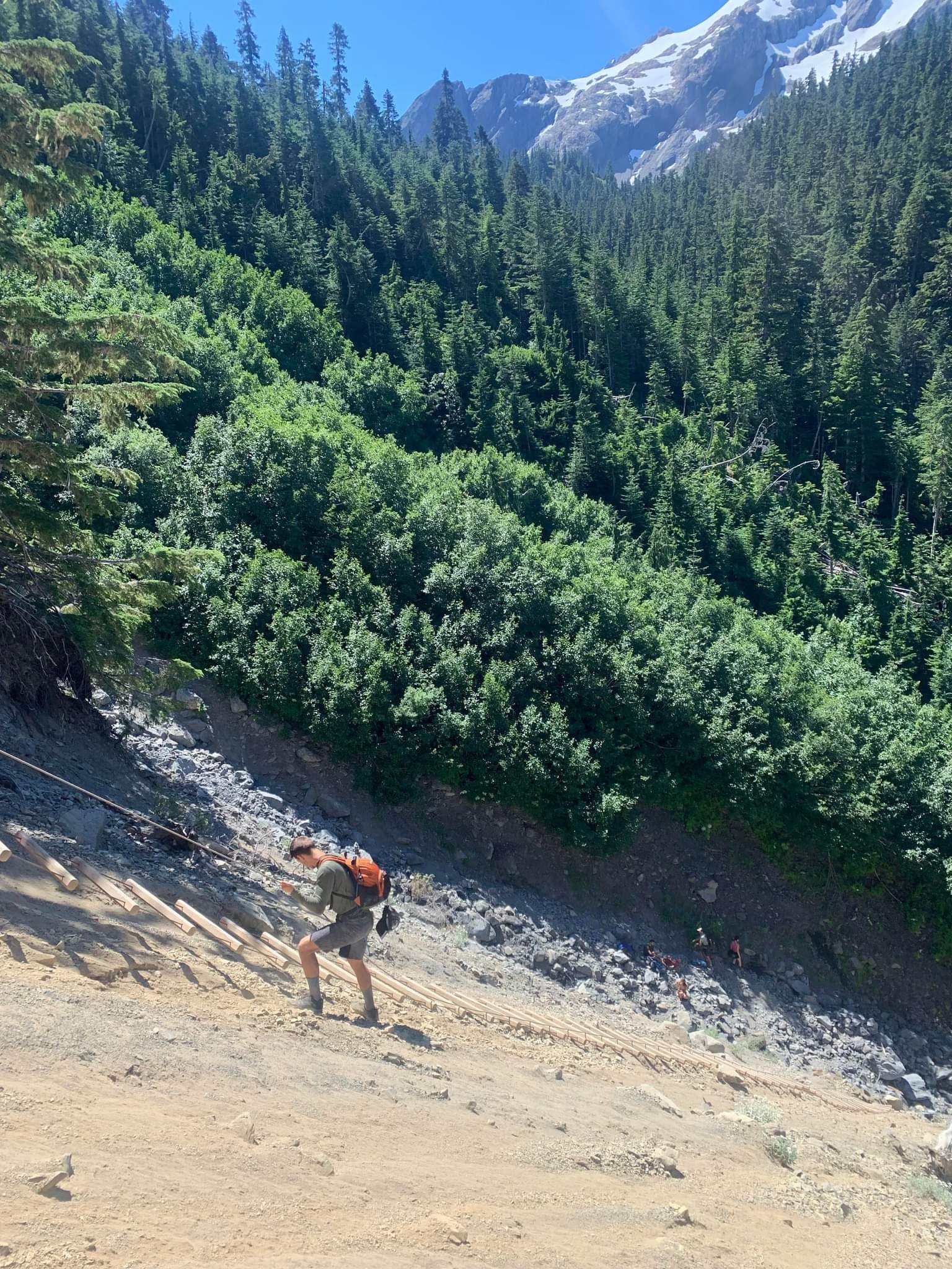 A photo of myself rappelling down a steep dirt and rock covered slope. I slowly work my way down with both hands on the rope.